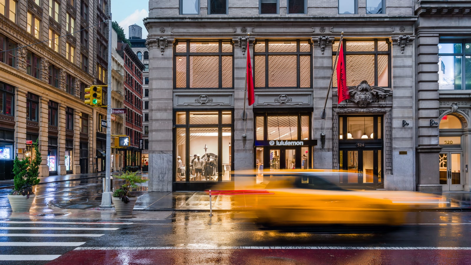 lululemon SoHo flagship on Broadway at dusk, with the storefront, red flags, and city movement visible.