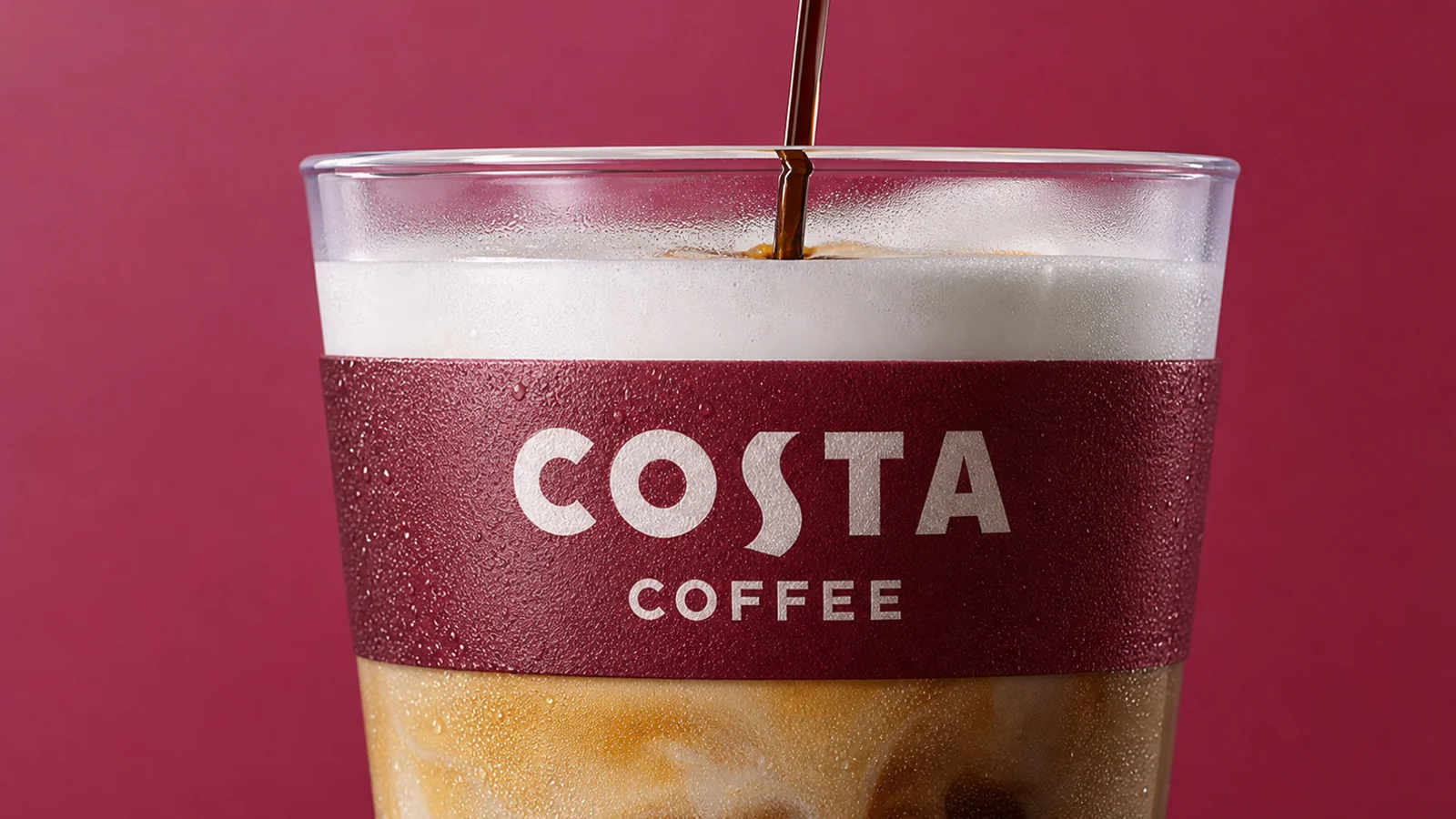 Layered Costa iced latte with a readable Costa Coffee sleeve against a burgundy background.