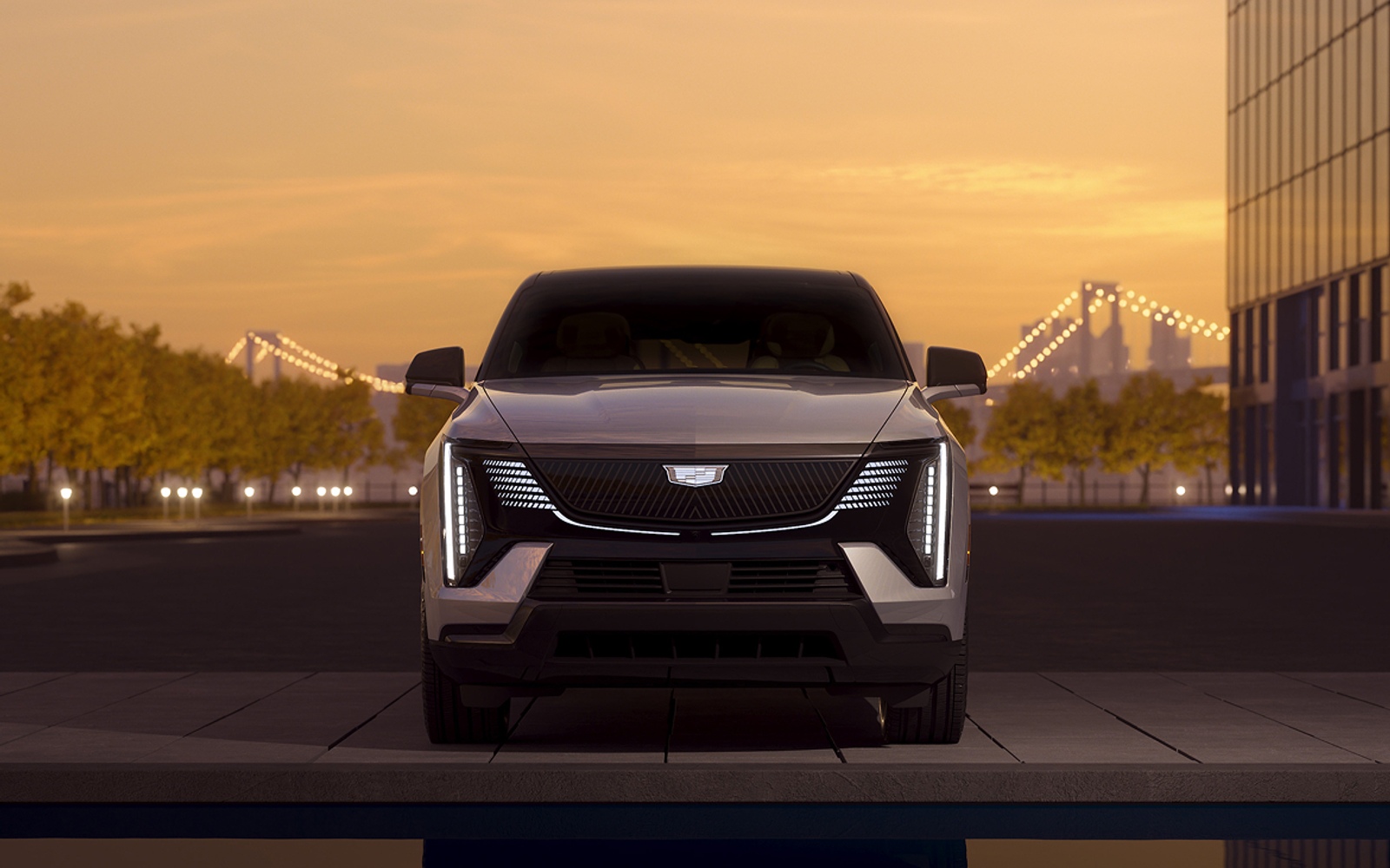 Cadillac electric SUV photographed from the front with city bridge and premium vehicle stance visible.