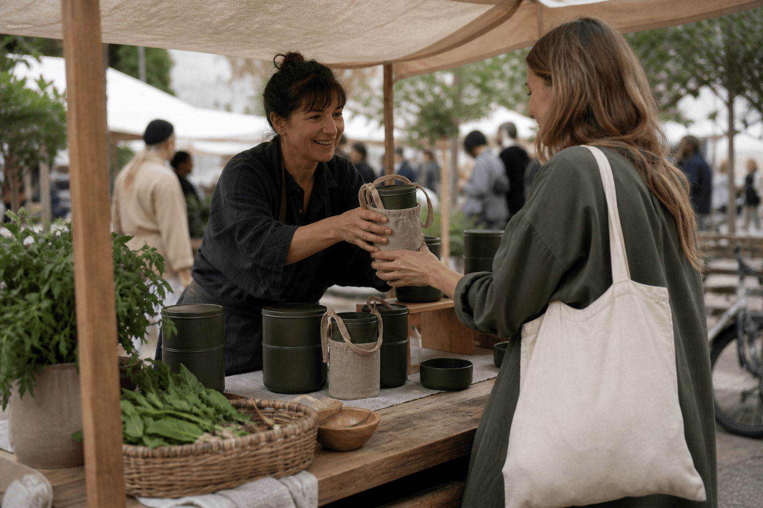 A maker handing the first buyer an unbranded reusable product at an outdoor market.