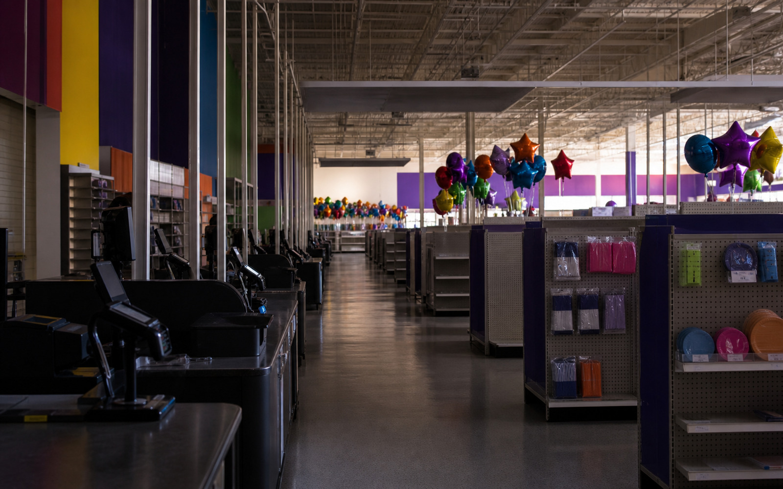 A darkened party-supply superstore with closed checkouts, partly cleared aisles, and unbranded balloon bouquets after liquidation.