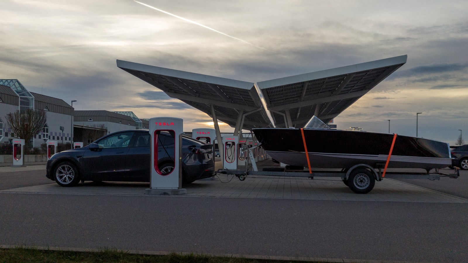 Tesla Supercharger site with vehicle charging under solar canopy.