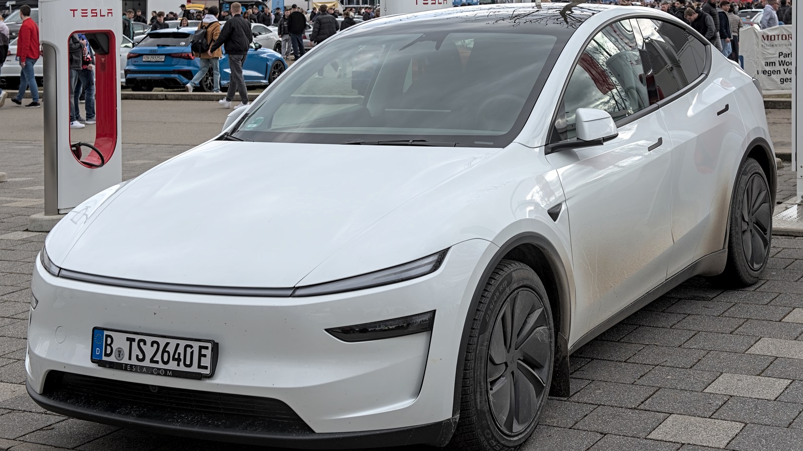 Tesla Model Y with Supercharger station visible behind it.