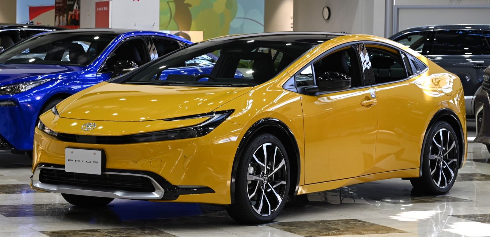 Yellow Toyota Prius plug-in hybrid in a showroom, showing the current product expression of Toyota's long hybrid lineage.