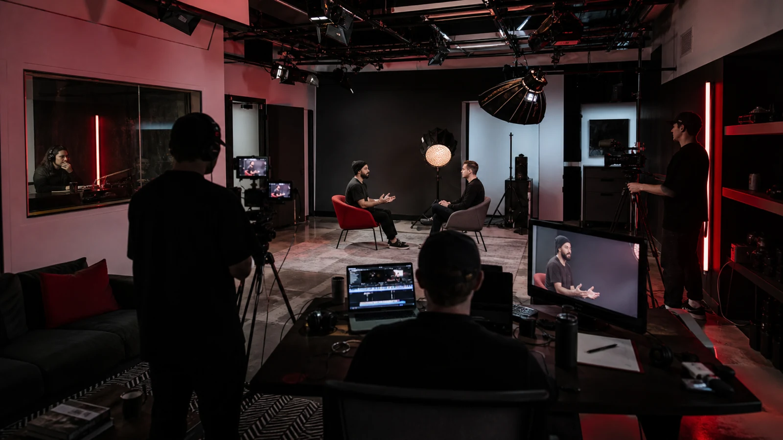 A compact logo-free creator studio producing a filmed interview under red and black lighting.
