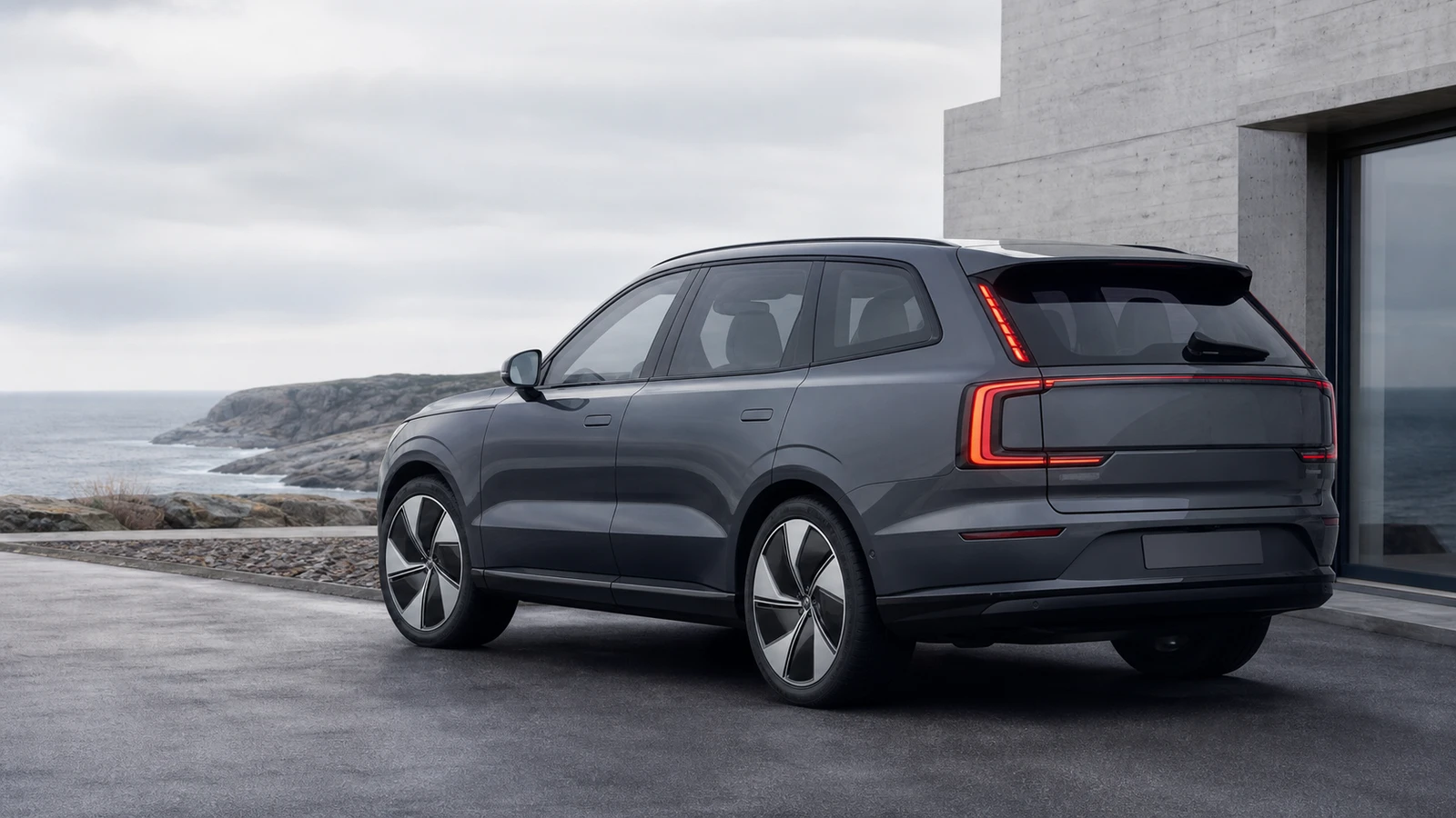 Logo-free charcoal electric family SUV beside minimal Nordic coastal architecture.