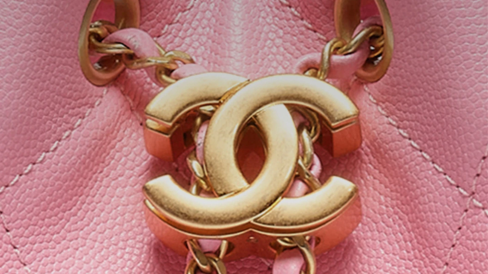 Close detail of double-C metal hardware, interlaced chain and quilting on a pink Chanel 25 bag.