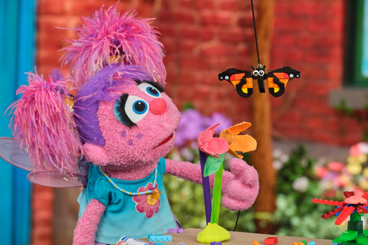 A Sesame Street character holds a craft flower beside a LEGO brick-built butterfly.