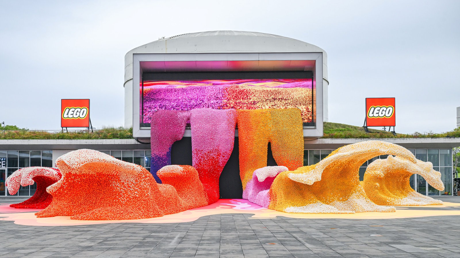 Pink, red and yellow waves of LEGO Botanicals outside the Tank Shanghai Art Centre, flanked by LEGO signs.
