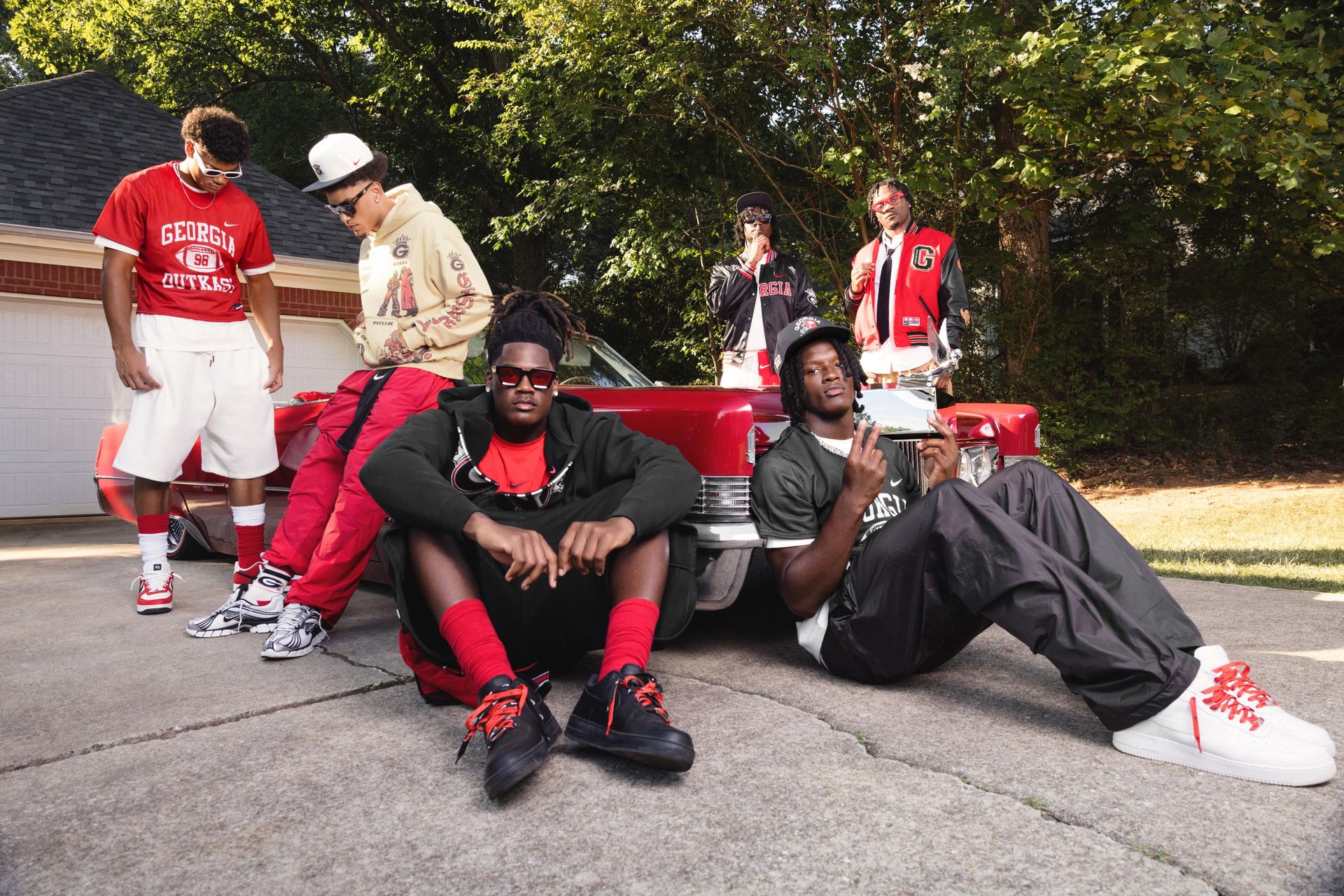 Six athletes wearing Nike's Georgia x Outkast collection around a red car.