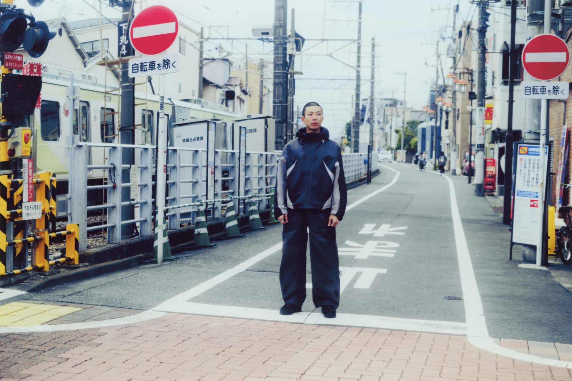 A model wearing a dark Nike Tech SF3 outfit beside a railway crossing.