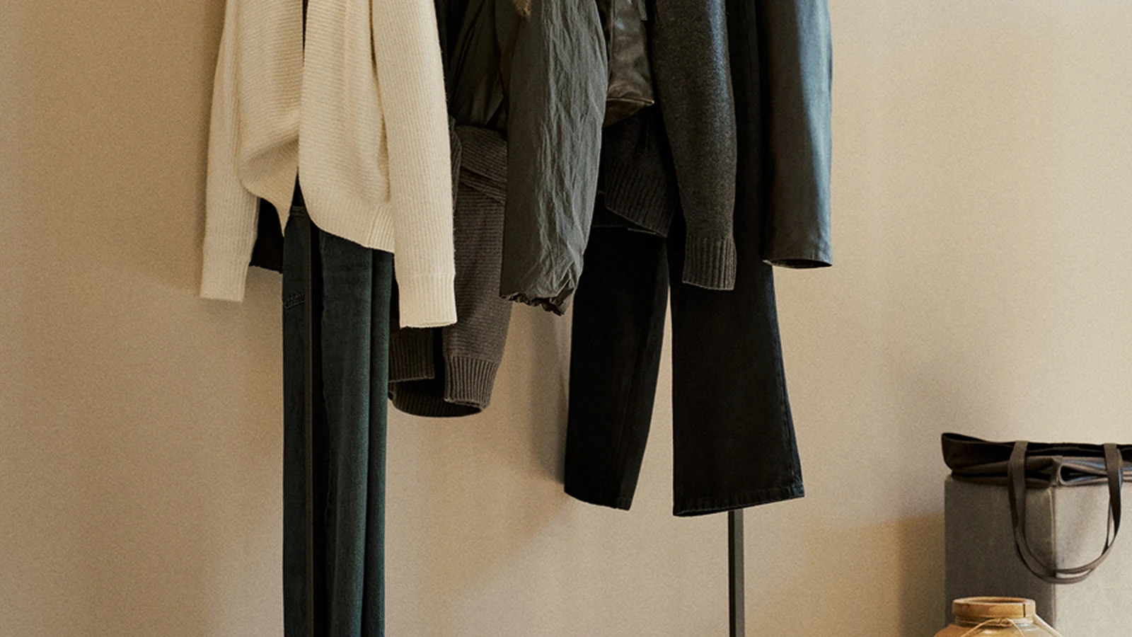 Massimo Dutti garments on a spare black rail beside a ceramic vessel.