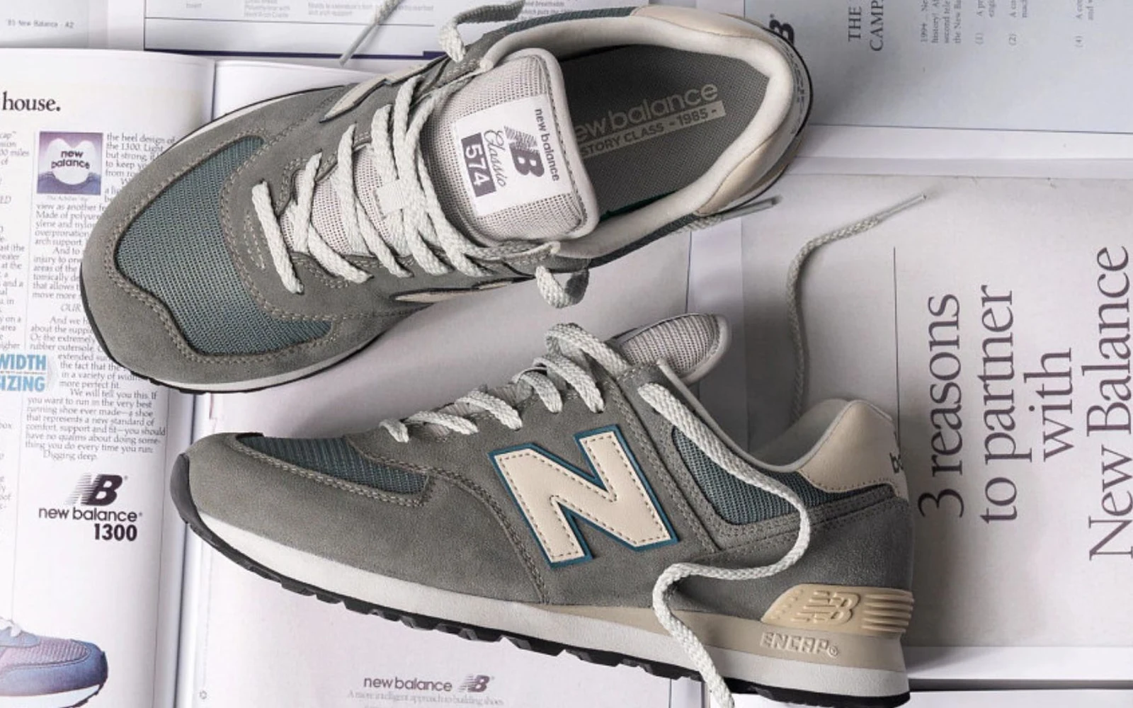 Grey New Balance shoes arranged over archival newspaper and product material.