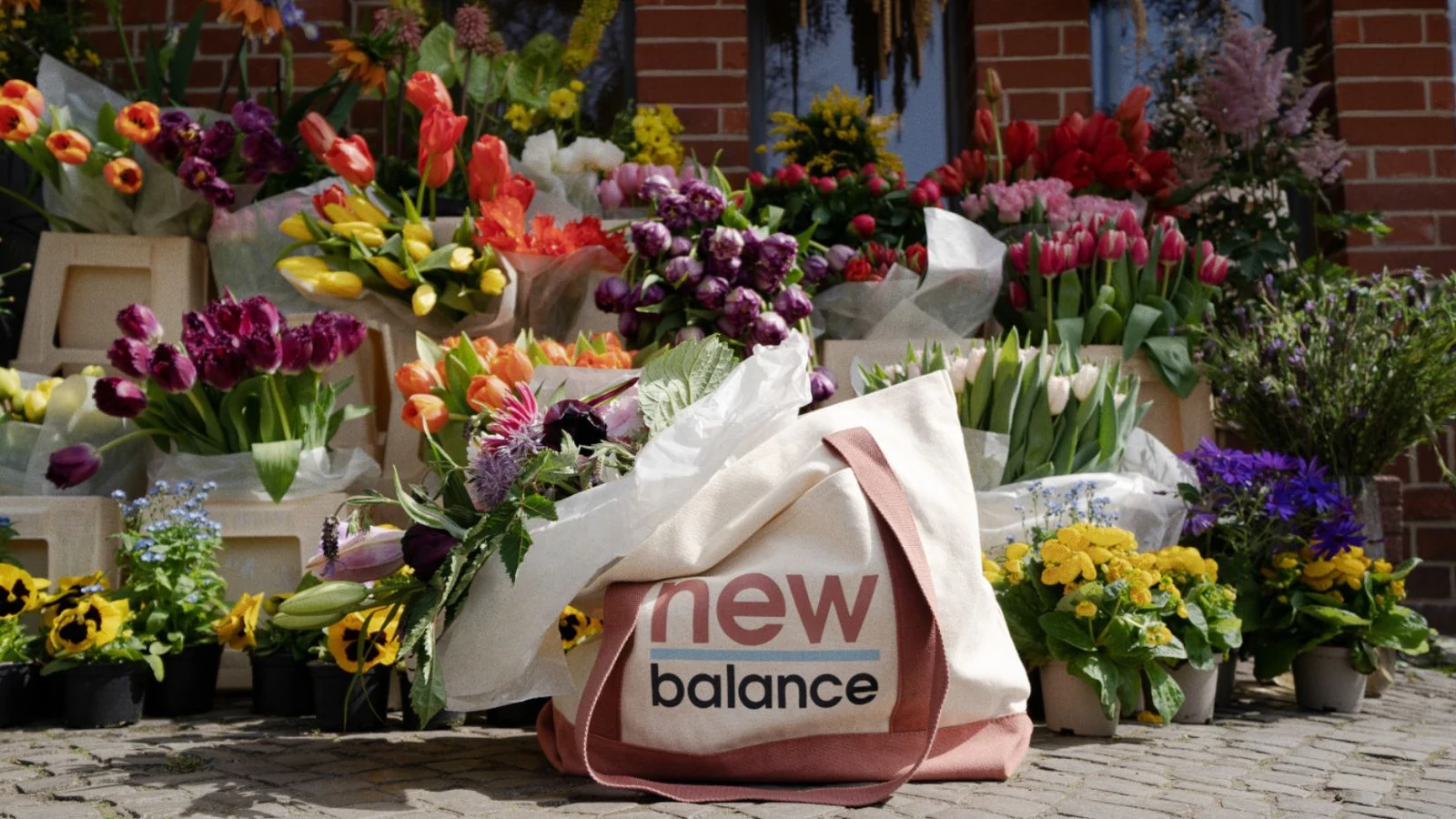 New Balance branded tote placed among a dense flower-market display.