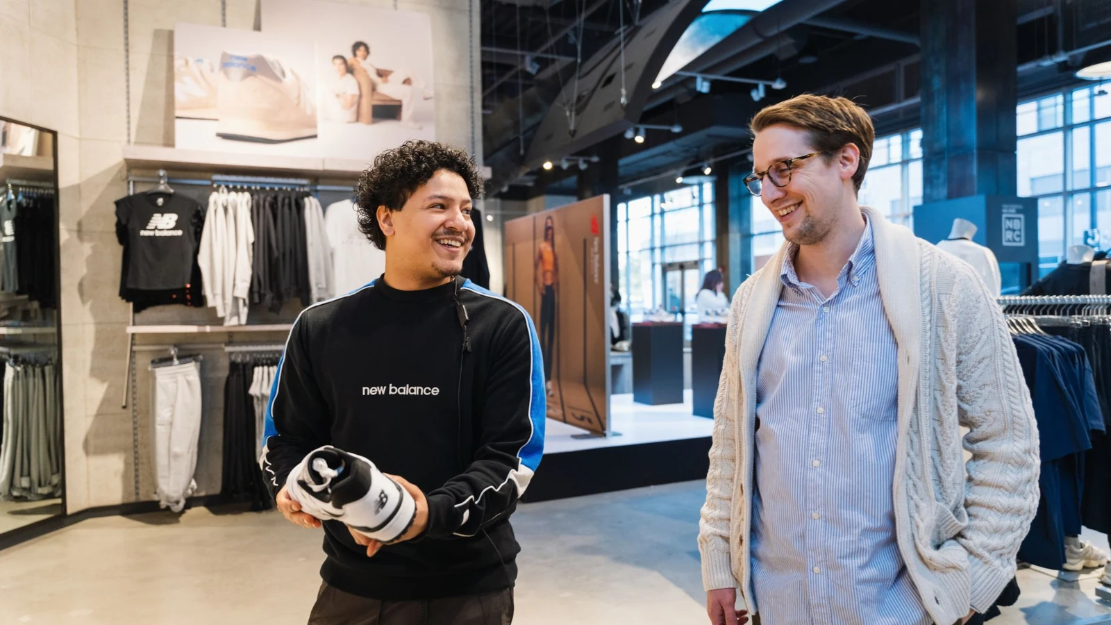 Two people holding a New Balance shoe inside a brand retail space.