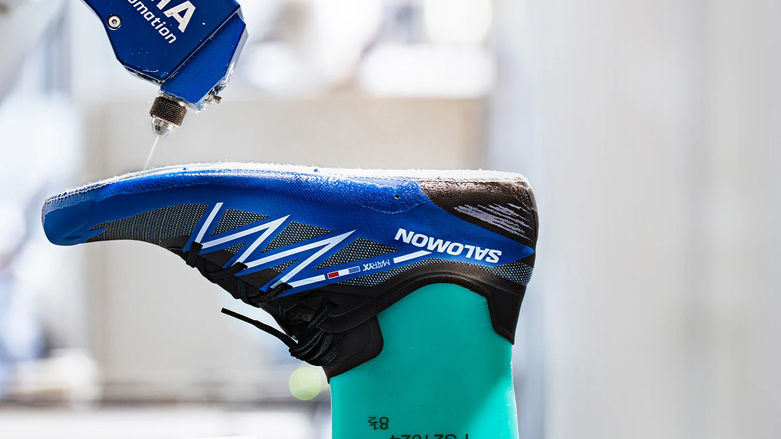 Automated footwear manufacturing arm holding a blue Salomon shoe.