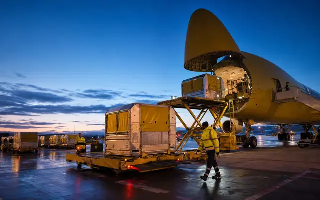 International air cargo hub at blue hour with yellow containers and active loading crews.
