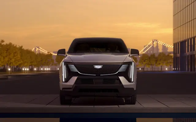 Cadillac electric SUV photographed from the front with city bridge and premium vehicle stance visible.